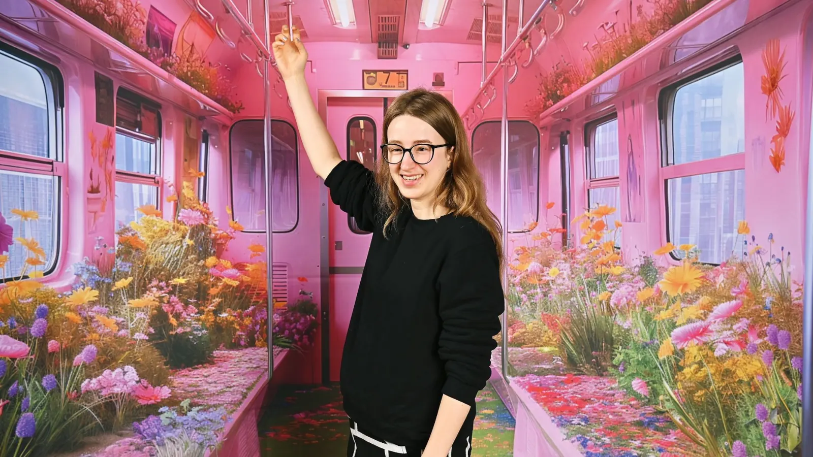 Luna Spiegel ríe con el brazo en alto, rodeada de una instalación artística de colores vivos con motivos florales.